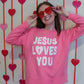 Person wearing a pink sweatshirt with 'Jesus Loves You' text, posing with heart-shaped sunglasses against a heart-patterned background.