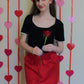 Woman holding a red rose against a heart-patterned background wearing a red skirt