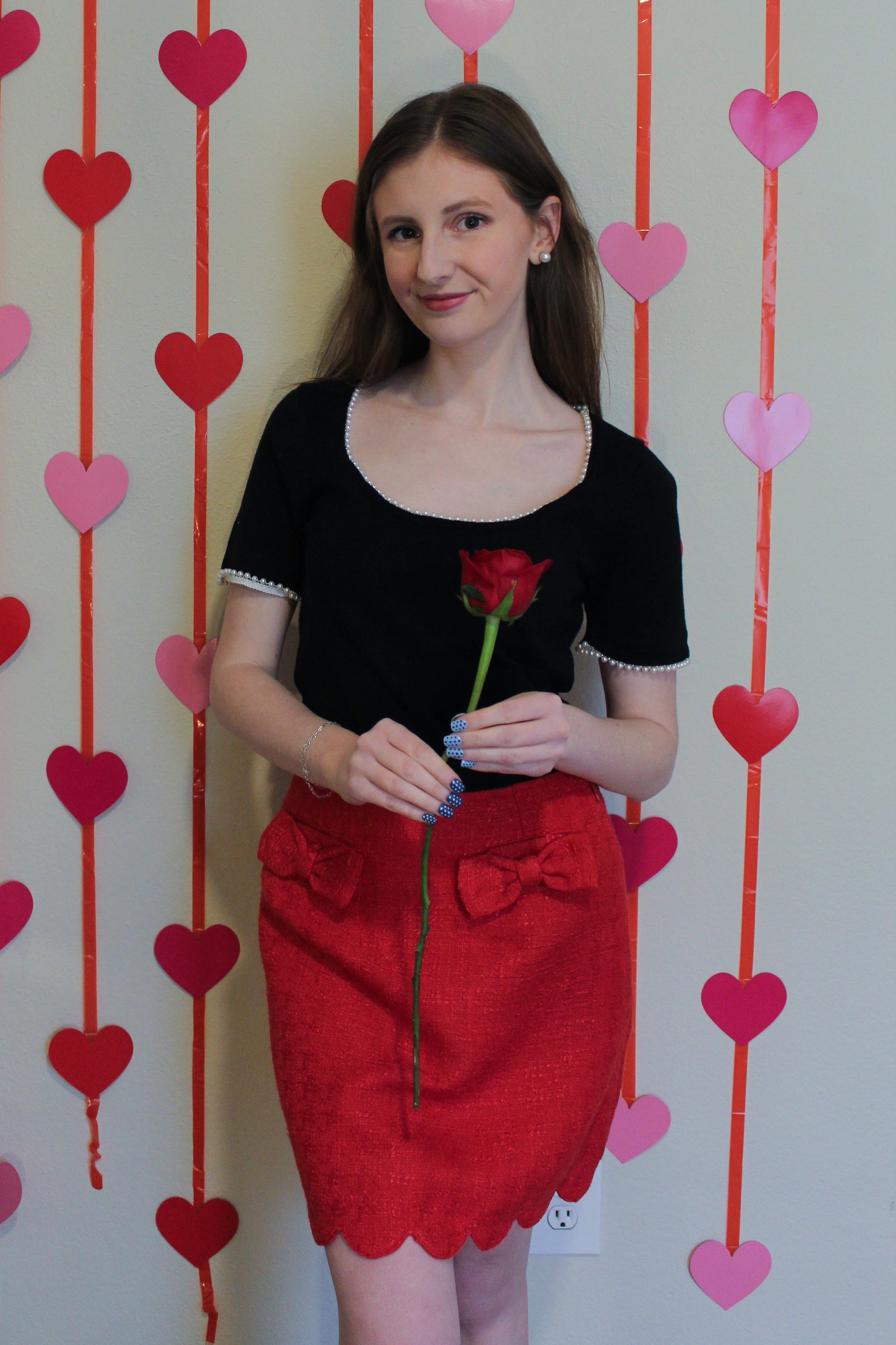 Woman holding a red rose against a heart-patterned background wearing a red skirt